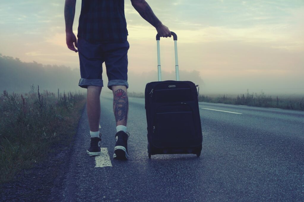 Man walking with a suitcase along a foggy road at sunrise, symbolizing adventure and travel.